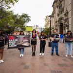 Seis personas de pie frente a una iglesia en una plaza, sosteniendo pancartas y carteles que dicen "LATAM Airlines: Deja de usar huevos de gallinas enjauladas" y "La crueldad no debería ser parte del catering".